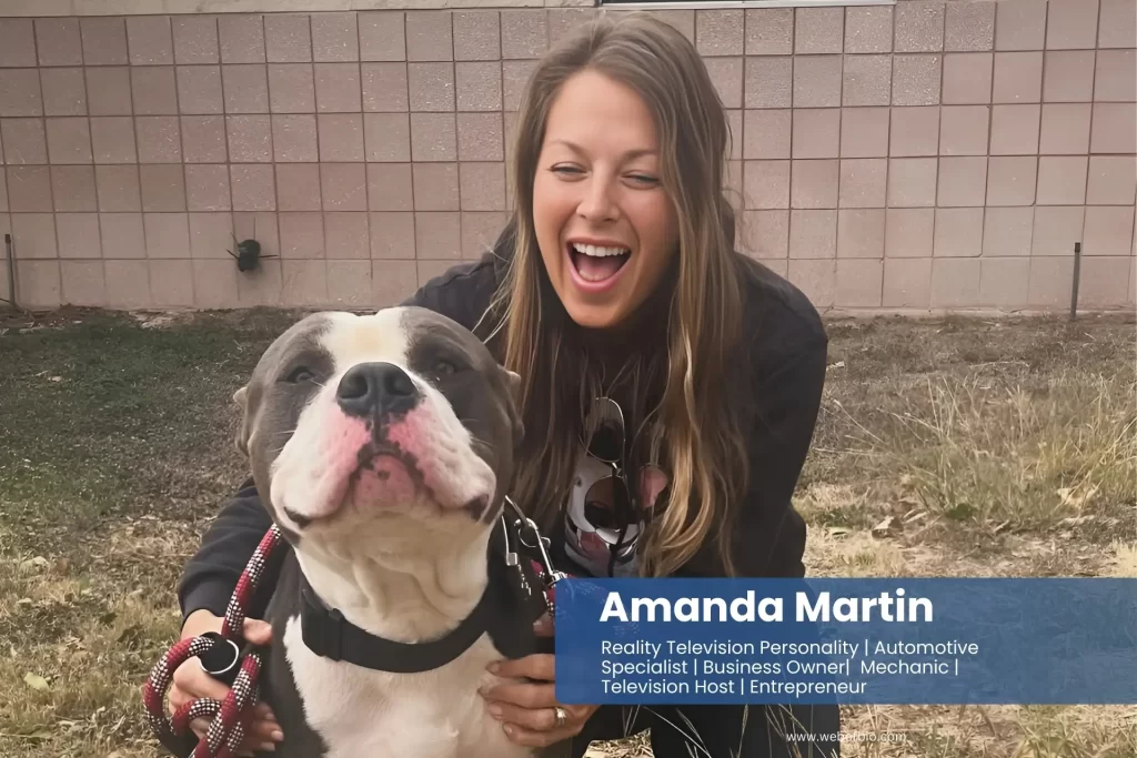 Amanda Martin poses with their dog in front of a brick wall.