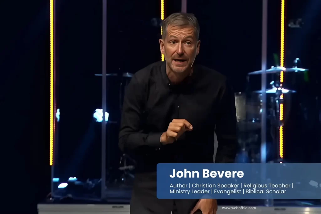 John Bevere in a black shirt is standing on stage.