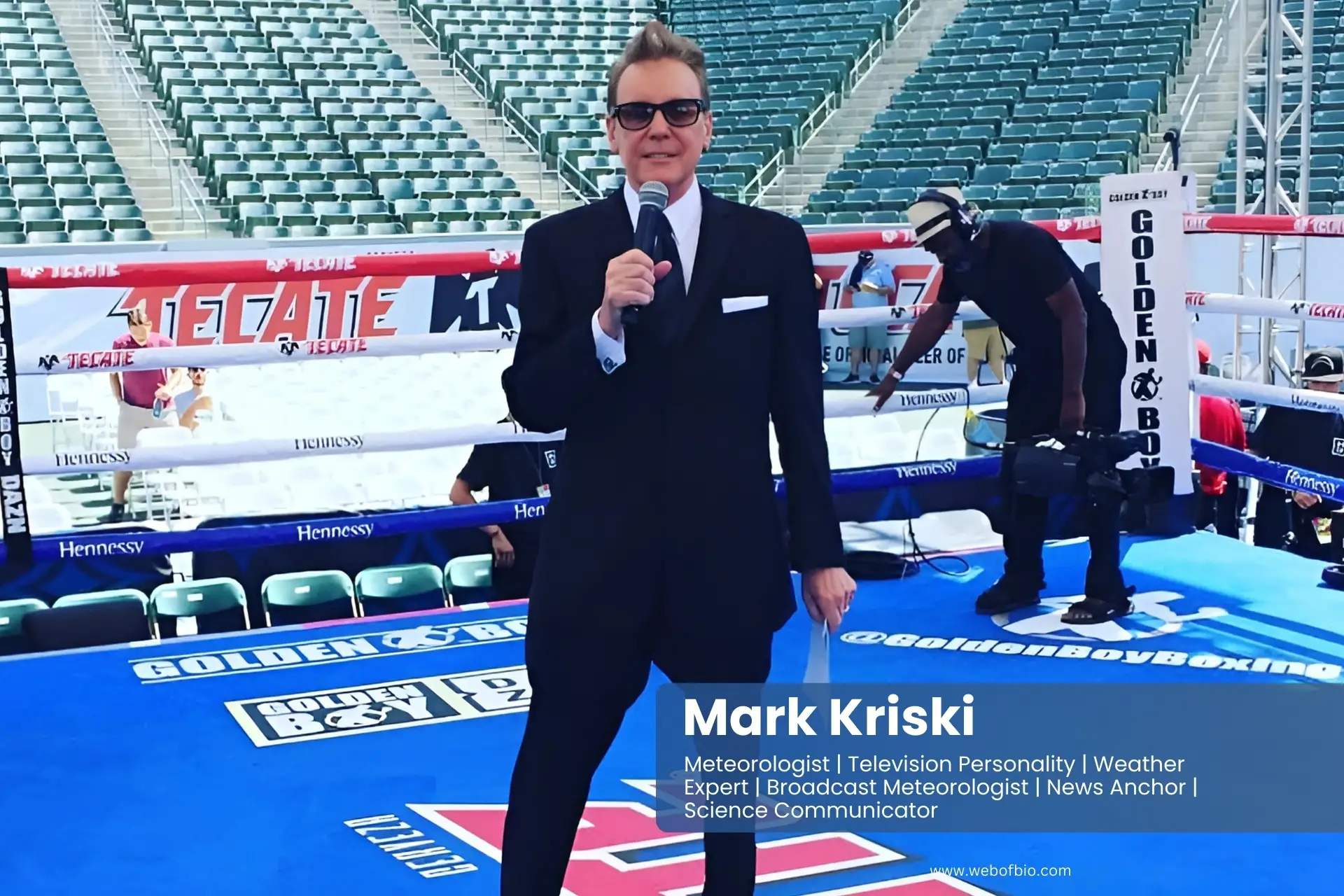 Mark Kriski in a suit and tie standing in front of a boxing ring.