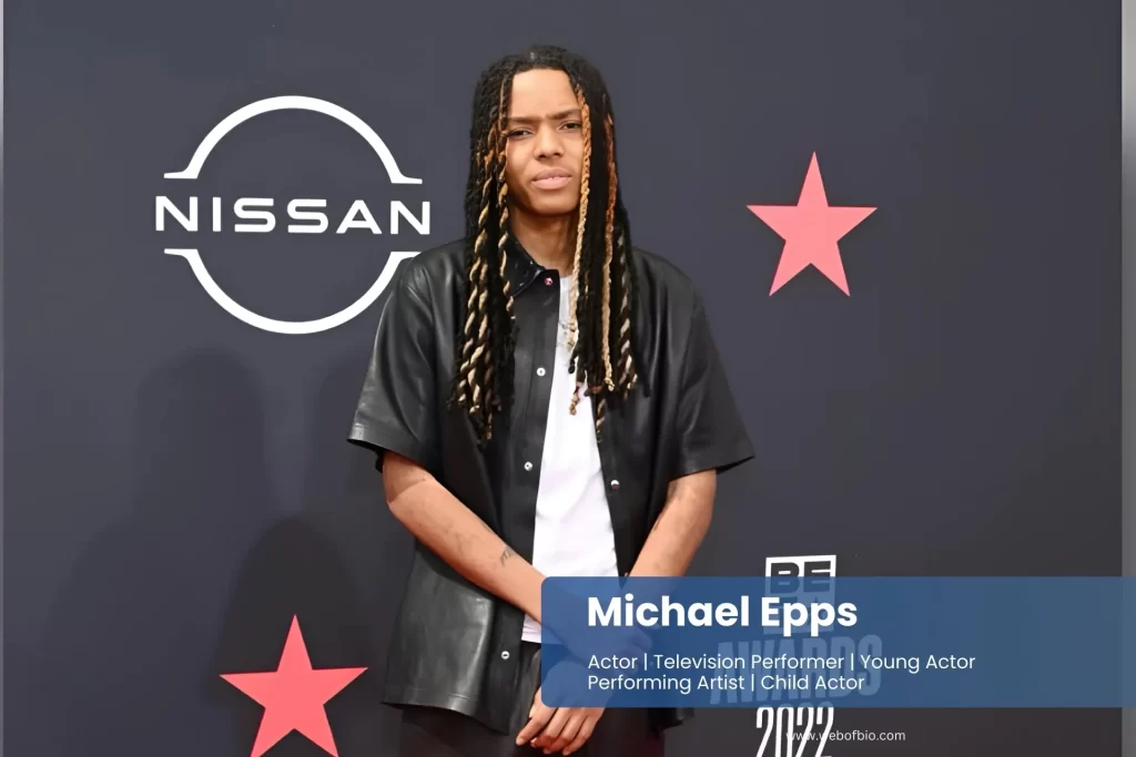 Michael Epps with dreadlocks standing on a red carpet.