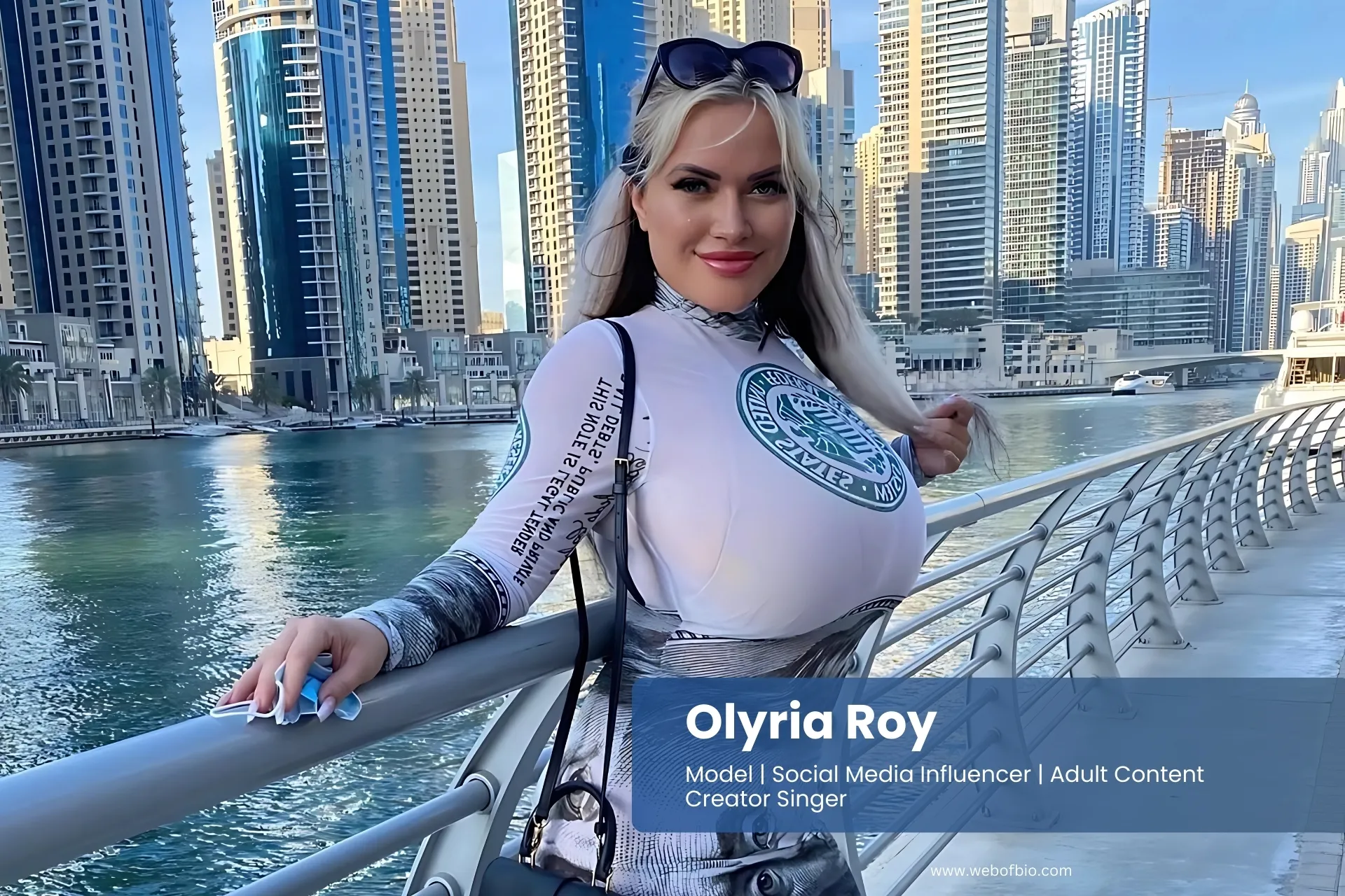 Olyria Roy is in a long dress and standing on a bridge in front of the city.