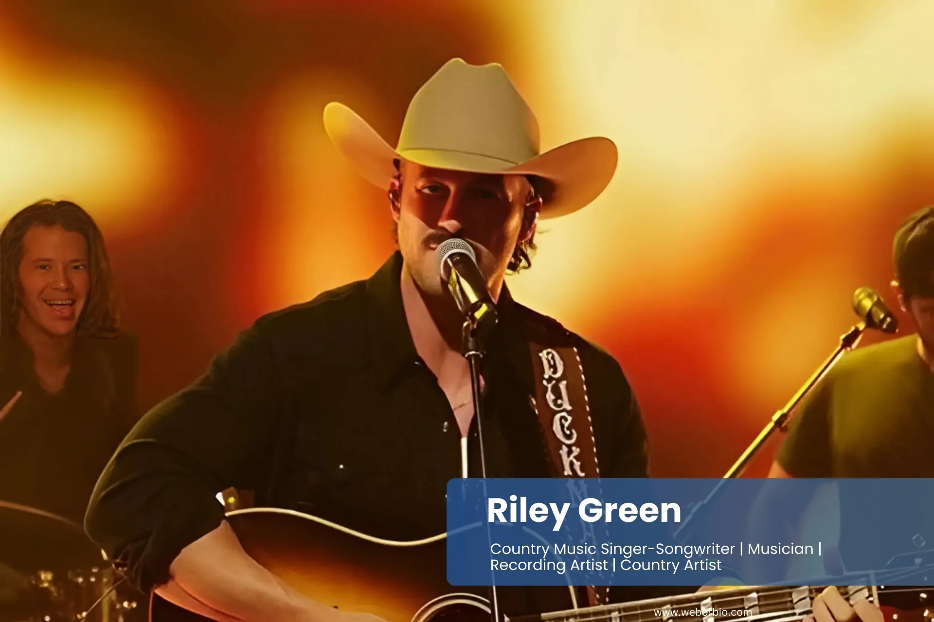 Riley Green in cowboy hat and sunglasses sings into a microphone, exuding confidence and charisma on stage.