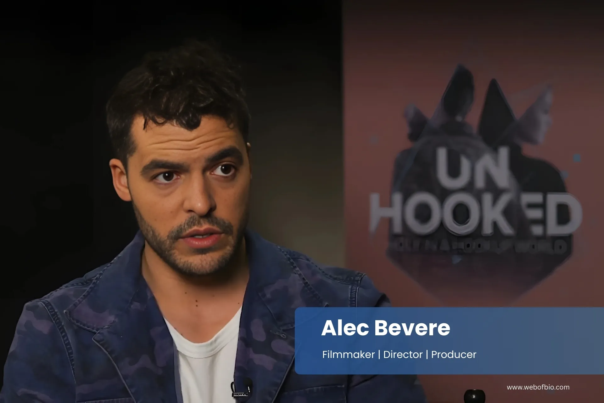 Alec Bevere is sitting in front of a wall with the words unhooked.