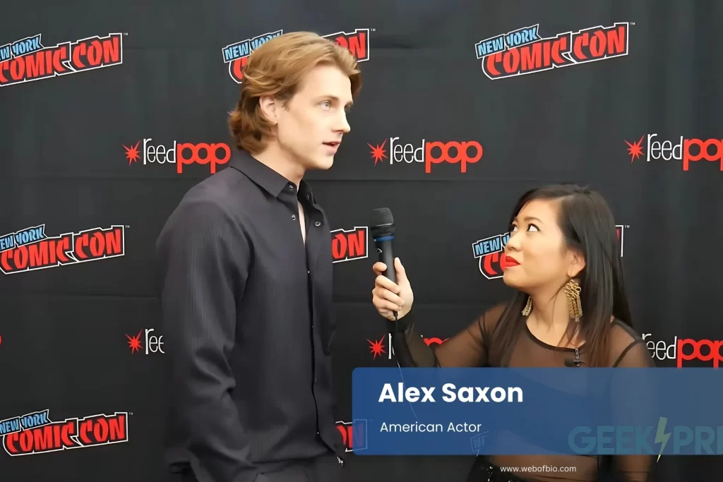 Alex Saxon engage with a reporter in conversation at a comic con, surrounded by colorful comic book displays and enthusiastic attendees.