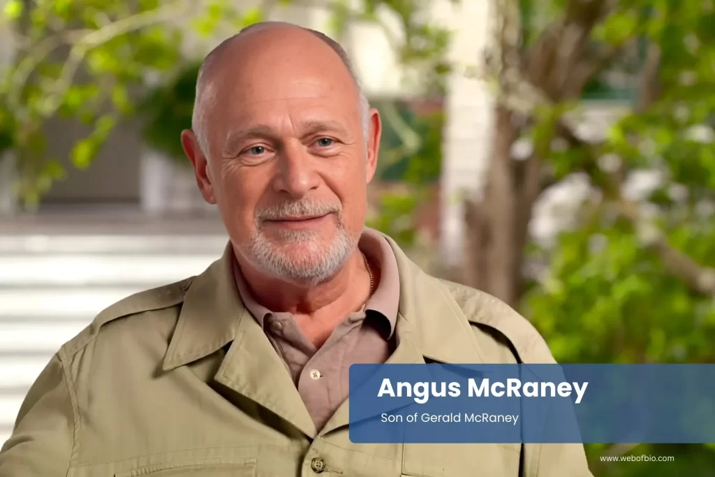Angus McRaney in a tan jacket standing in front of a house.
