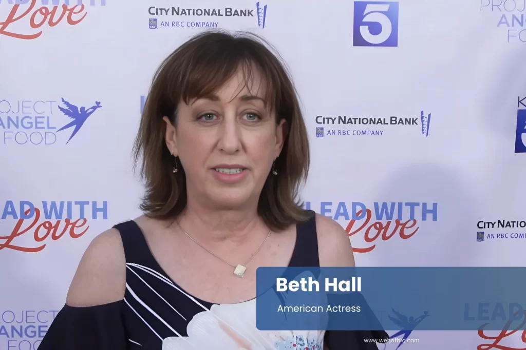 Beth Hall in formal attire stands confidently in front of a vibrant red carpet, ready for a special event.