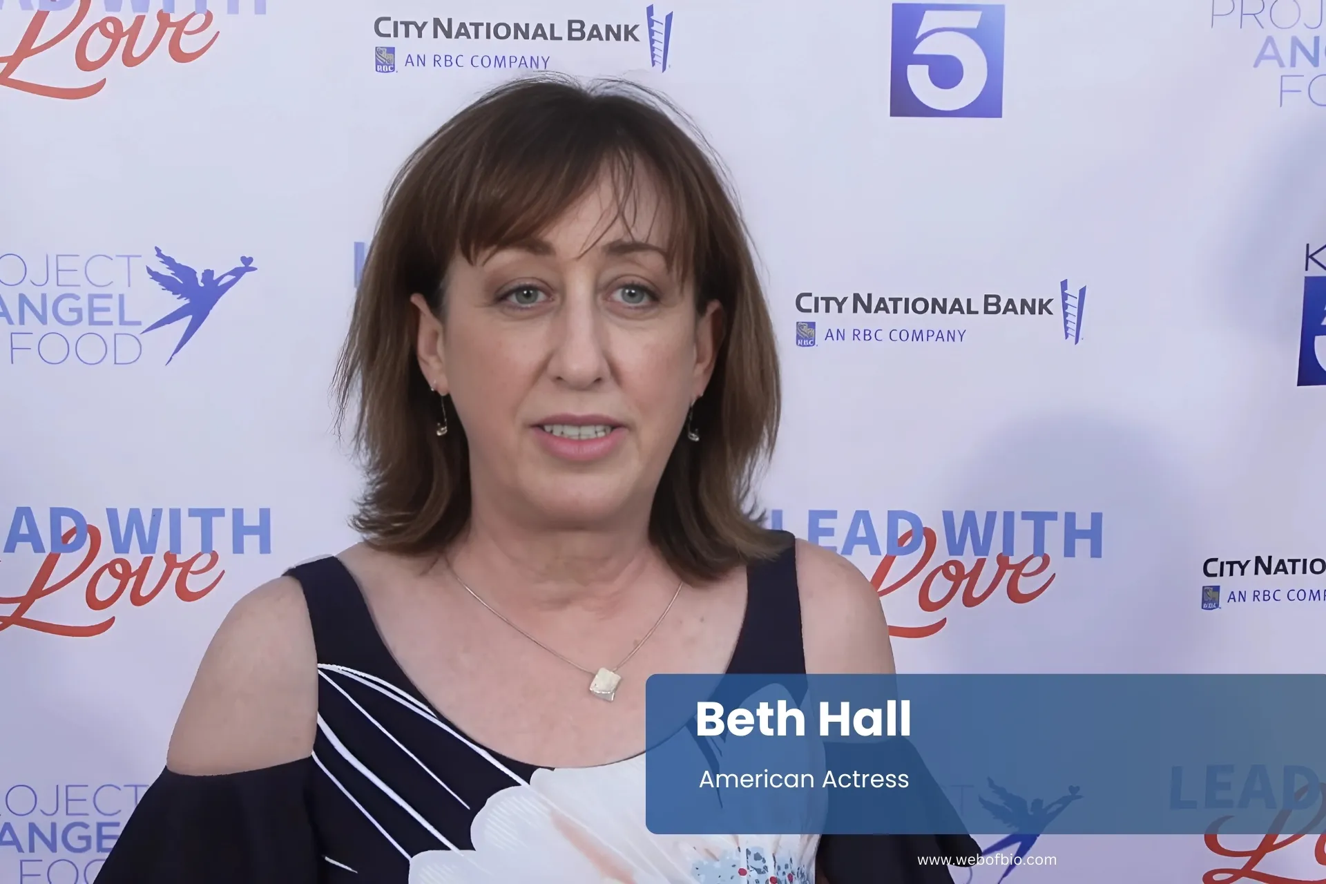 Beth Hall in formal attire stands confidently in front of a vibrant red carpet, ready for a special event.