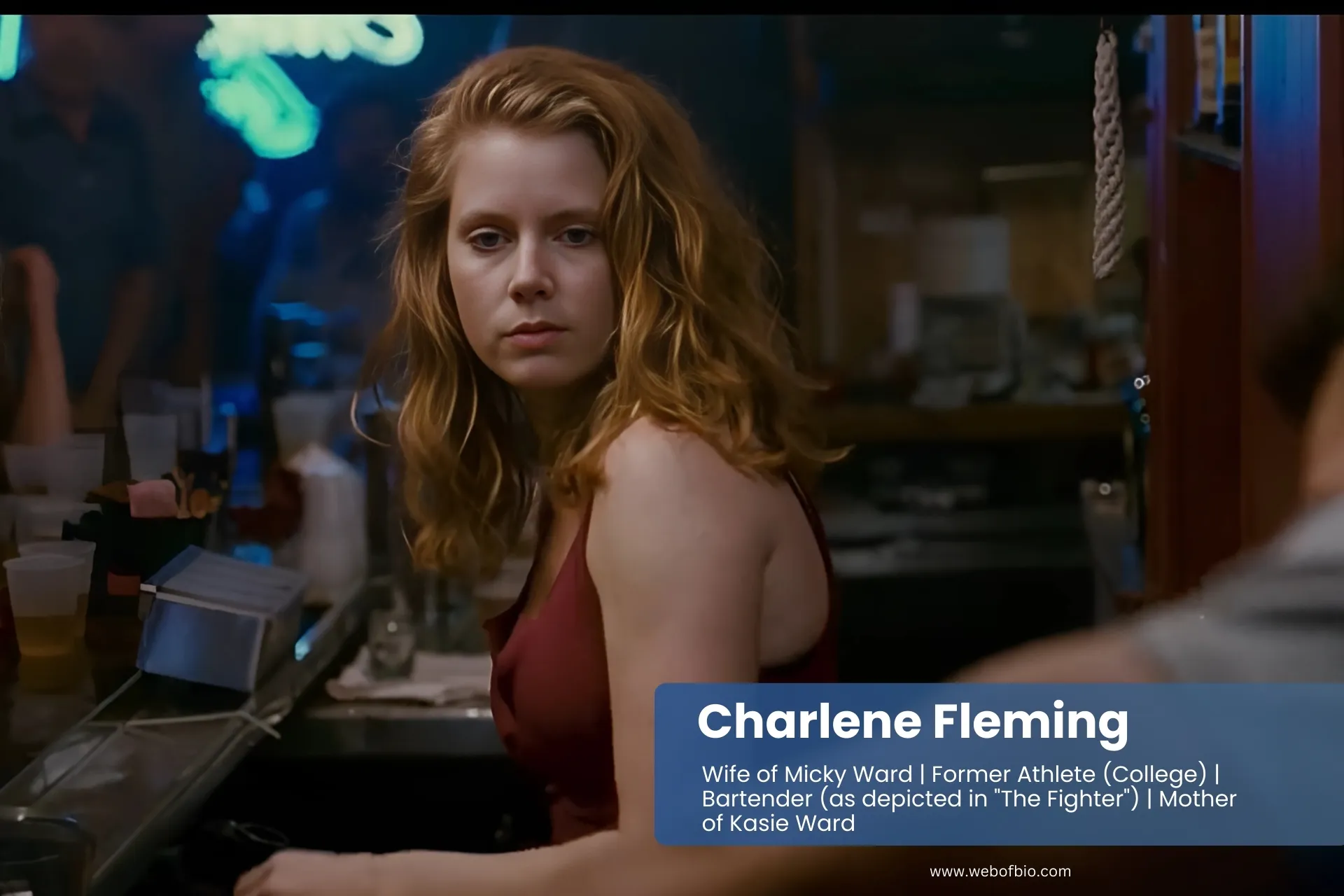 Charlene Fleming in a red dress sits at a bar, looking thoughtfully at her drink in a dimly lit setting.
