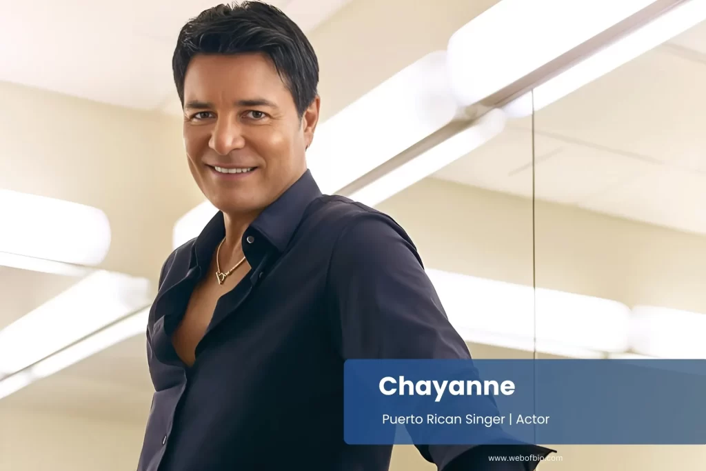 Chayanne wearing a black shirt leans against a counter, showcasing a relaxed demeanor in a casual setting.