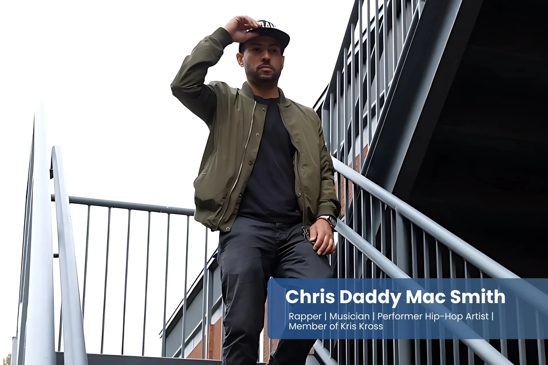 Chris Daddy Mac Smith is standing on some stairs, wearing black pants and a green jacket.