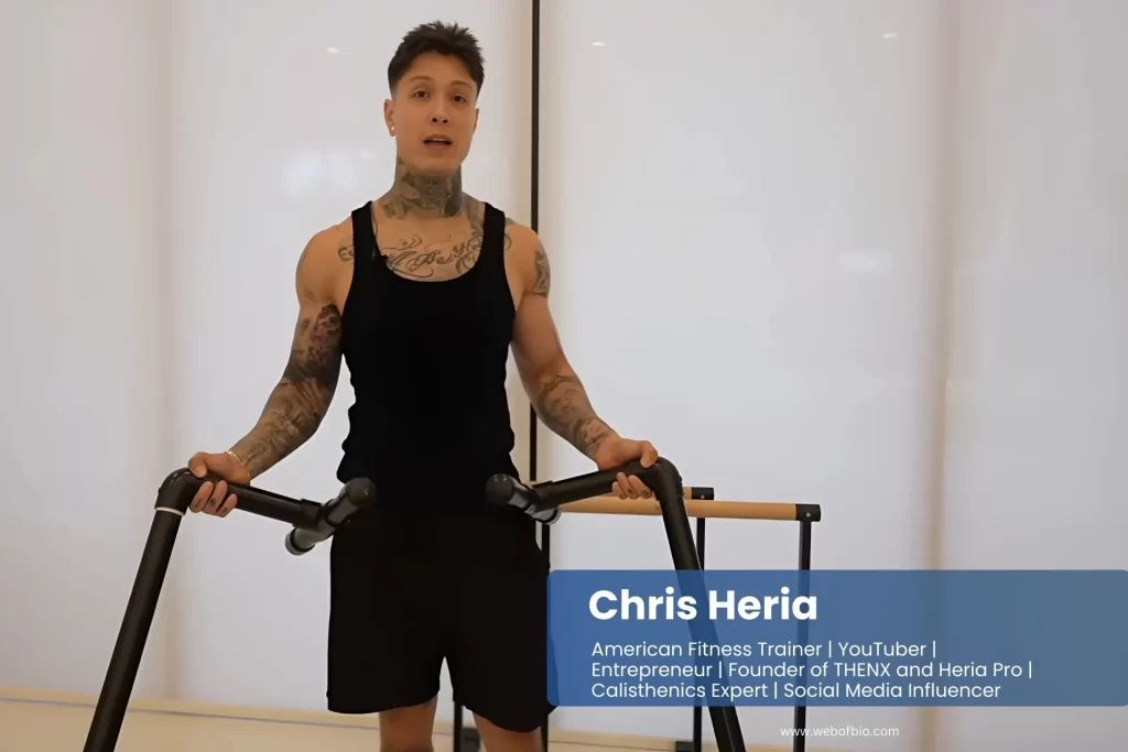 Chris Heria with tattooed arms pedals on a stationary bike, focused on his workout in a bright gym setting.