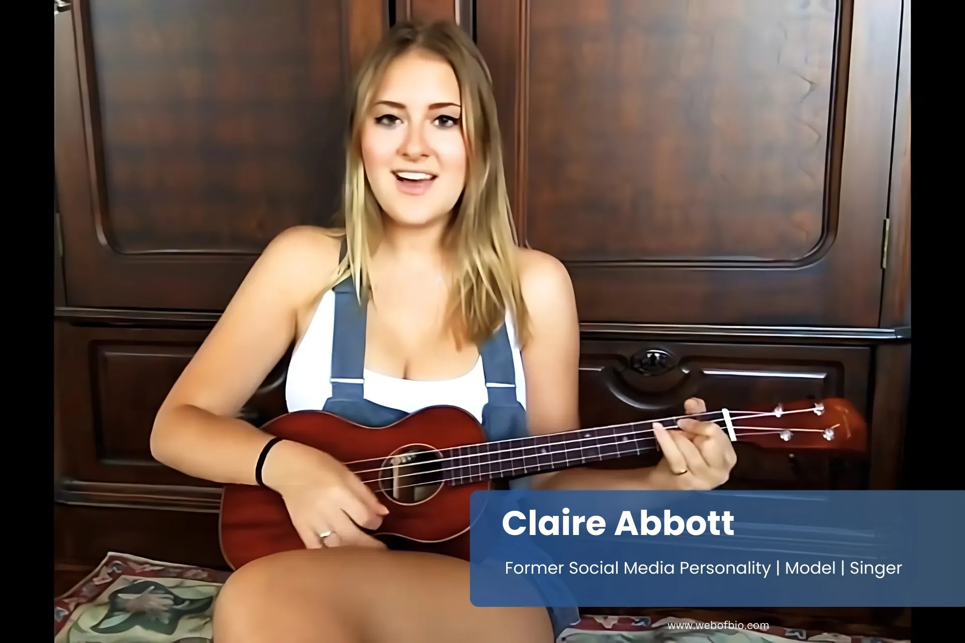 Claire Abbott sits on a couch, playing a ukulele with a joyful expression on her face.
