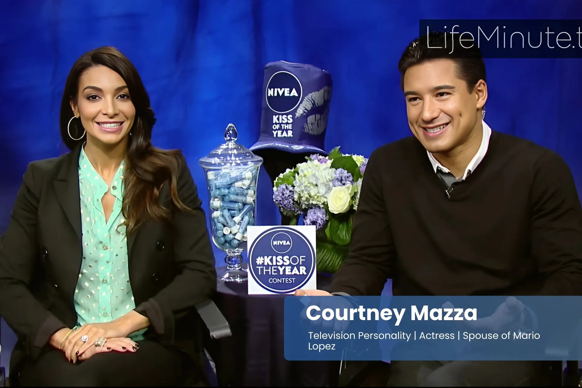 Courtney Mazza and Mario Lopez sitting next to each other on a blue couch