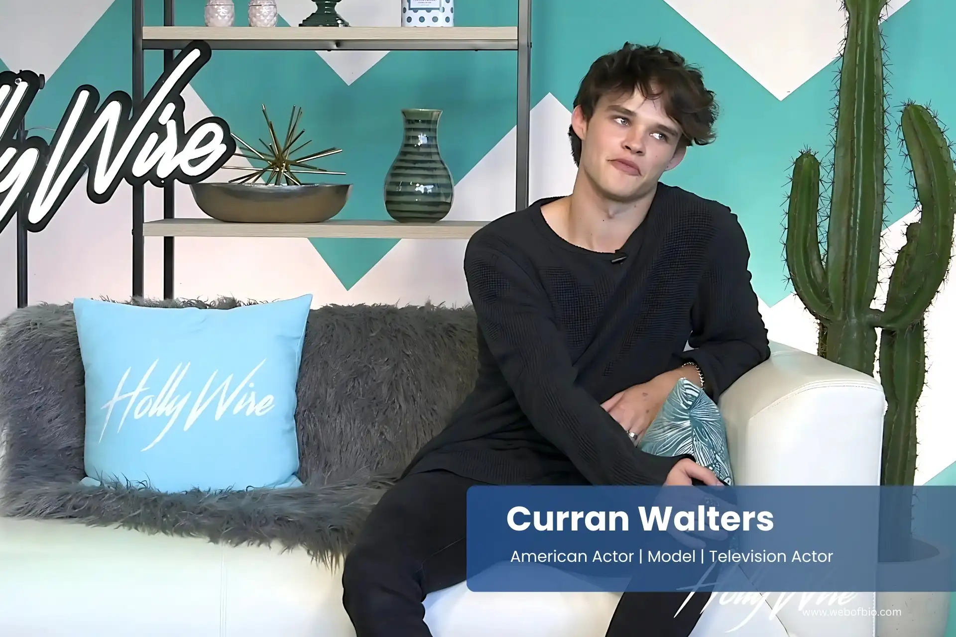 Curran Walters sitting on a couch in front of a cactus.