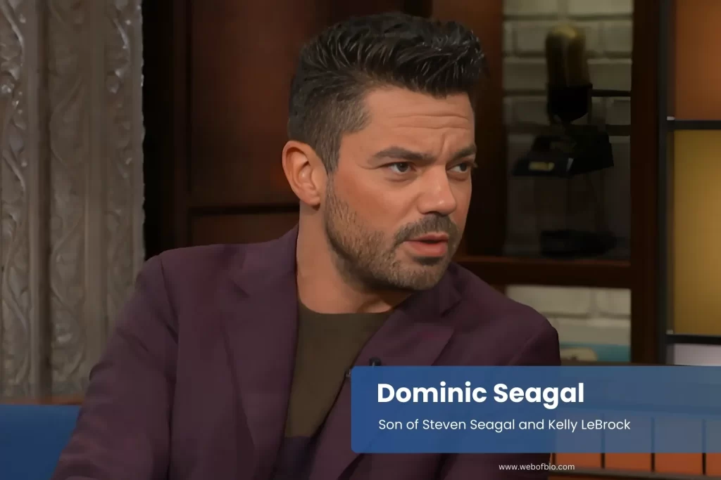 Dominic Seagal in suit sitting comfortably on couch.