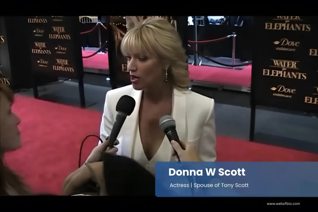 Donna W Scott in a white blazer talking to reporters on the red carpet.