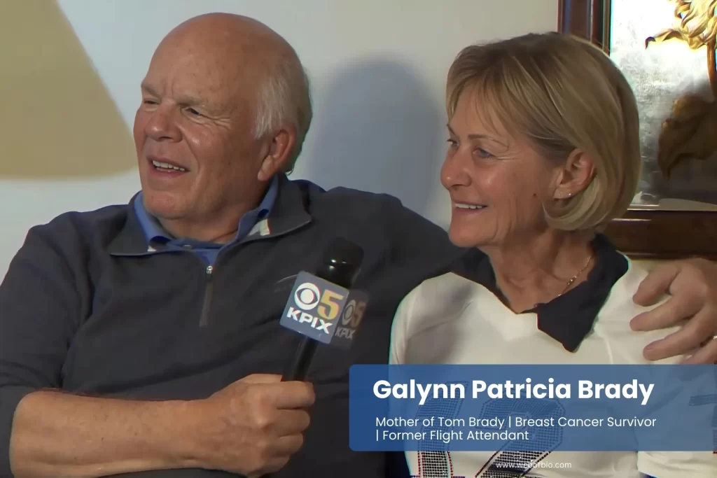 Galynn Patricia Brady and her husband sit on a couch, smiling and holding a microphone, engaged in a joyful conversation or performance.