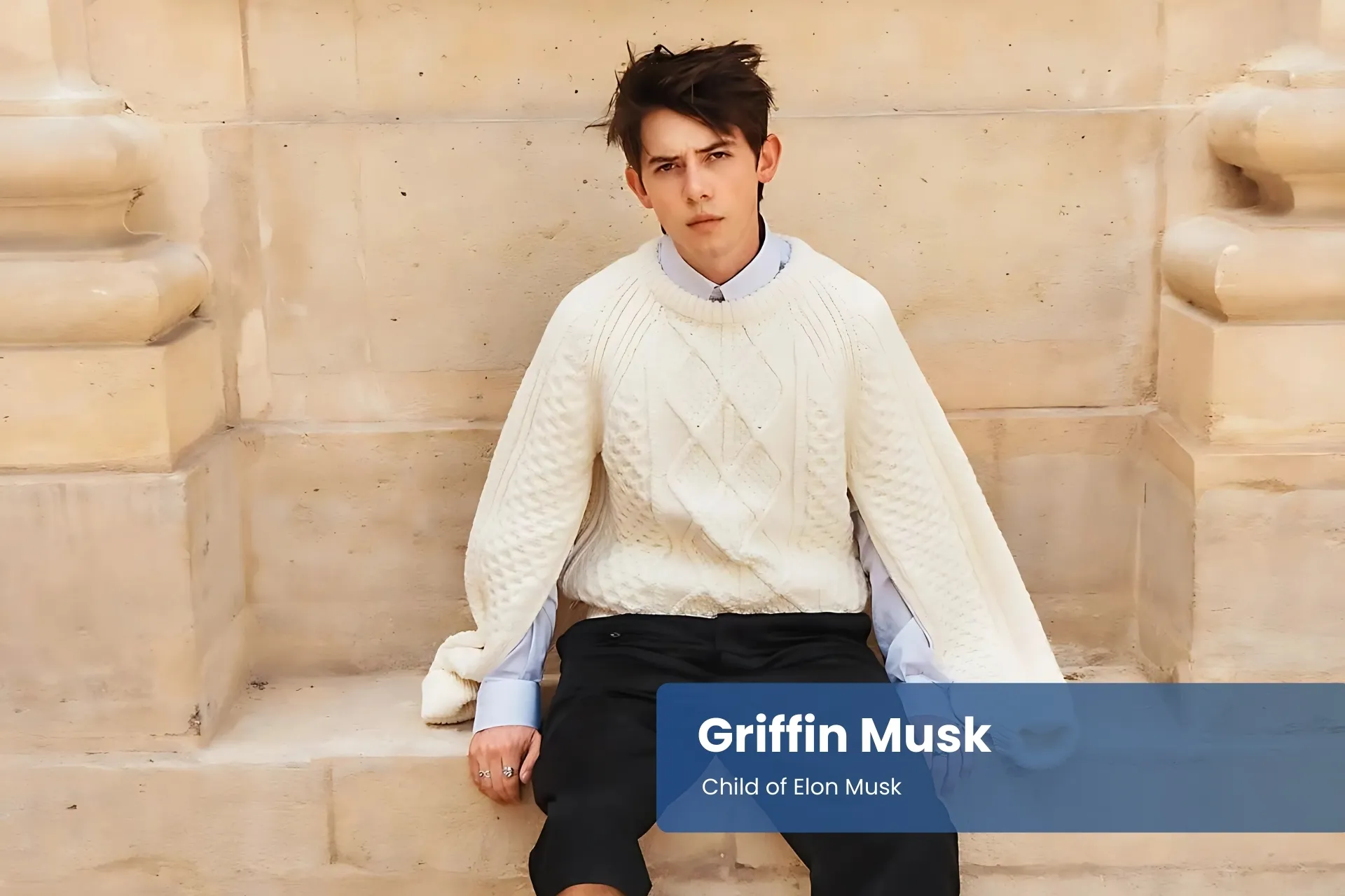 Griffin Musk sitting on steps wearing a white sweater and black pants.