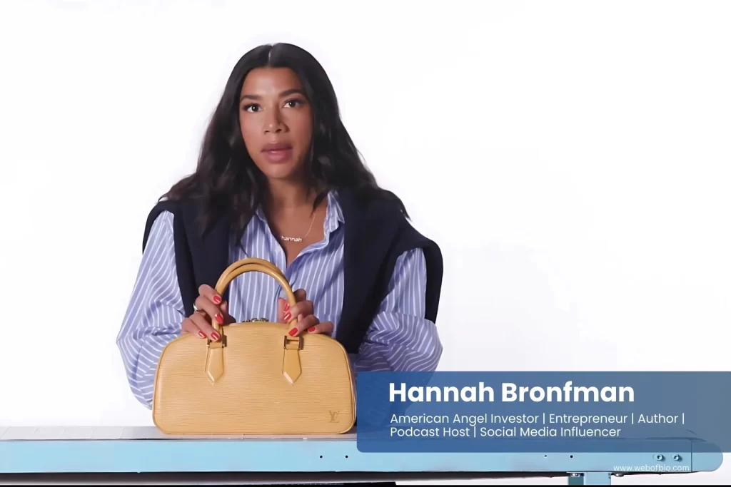 Hannah Bronfman is sitting at a table holding a handbag.