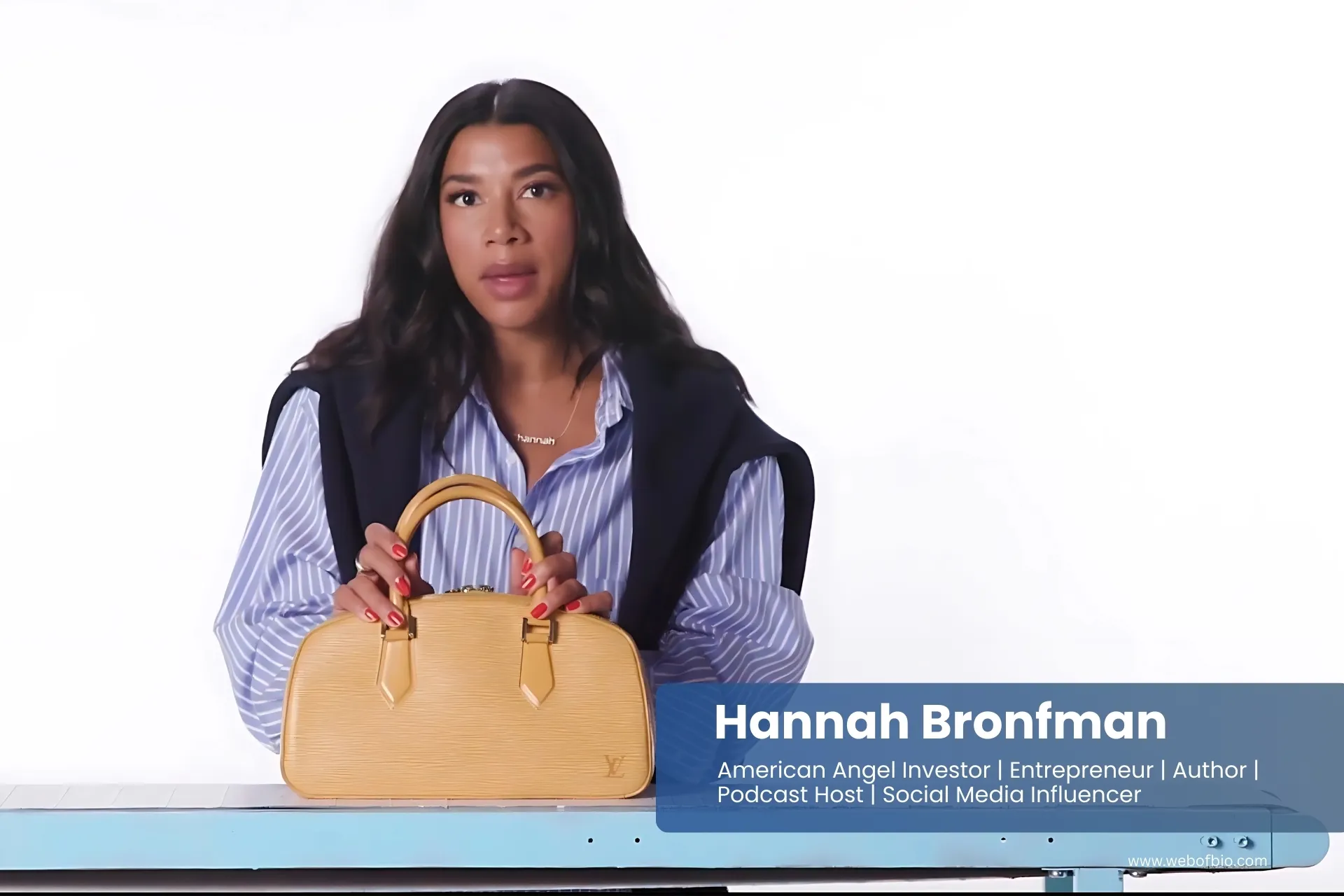 Hannah Bronfman is sitting at a table holding a handbag.