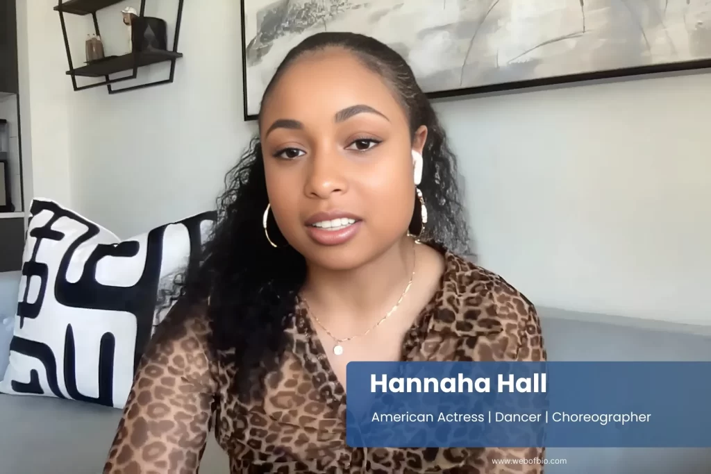 Hannaha Hall, wearing a leopard-print shirt, sits comfortably on a couch, smiling and relaxed in a cozy living room setting.