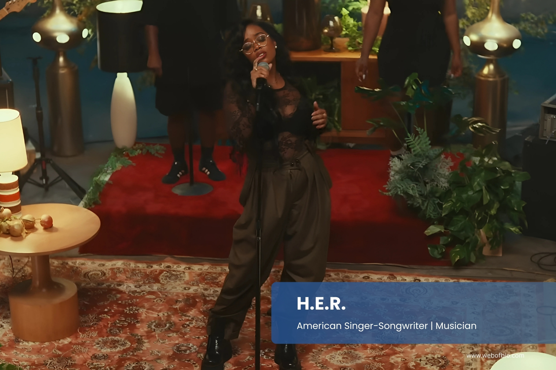 H.E.R. singing into a microphone in front of a group of people.