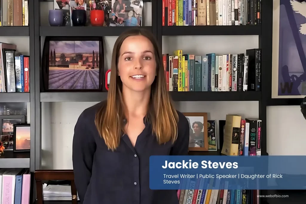 Jackie Steves is standing in front of a bookshelf full of books.