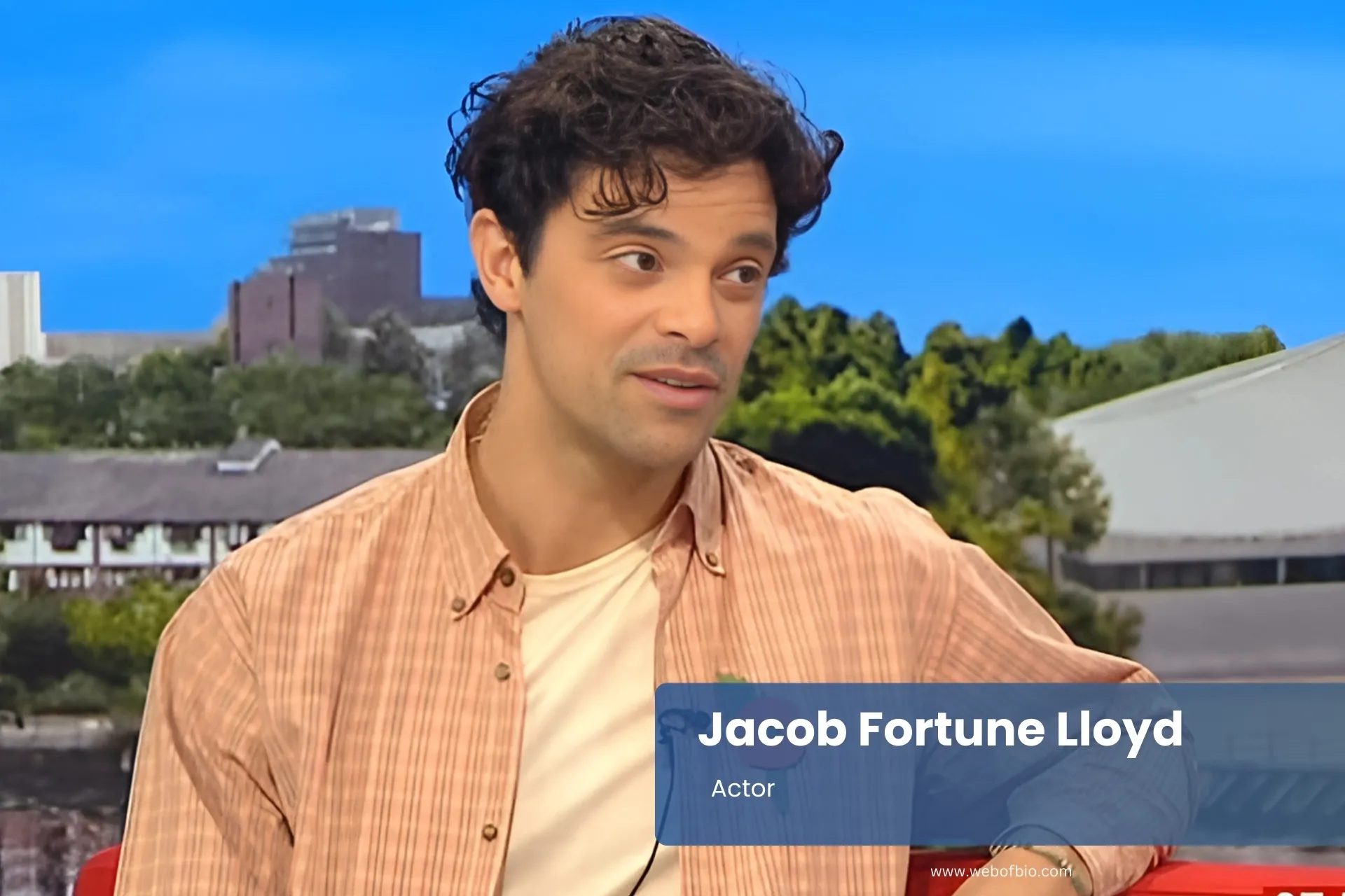 Jacob Fortune Lloyd sitting on red couch holding camera.