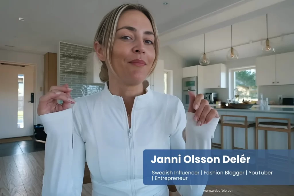 Janni Olsson Delér, wearing a white shirt, sits at a table, engaged in conversation or contemplation.