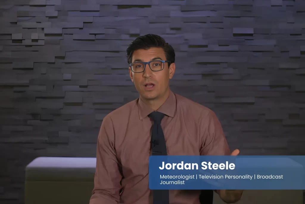 Jordan Steele wearing glasses and a tie sitting on a couch.