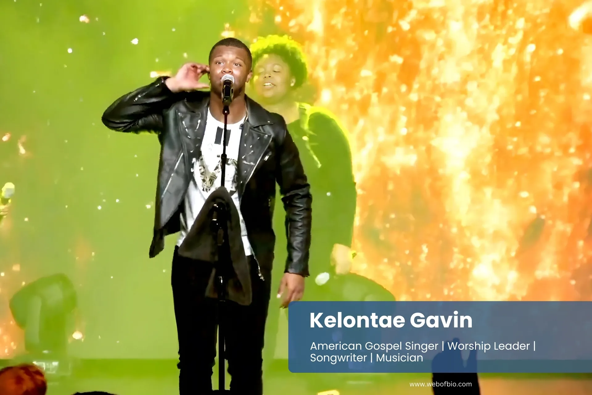 Kelontae Gavin, in a black jacket, stands on stage, addressing a large crowd of people in an auditorium.