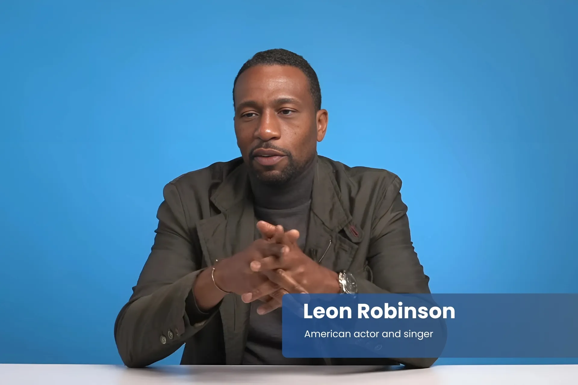 Leon Robinson sitting at a table in front of a blue background.
