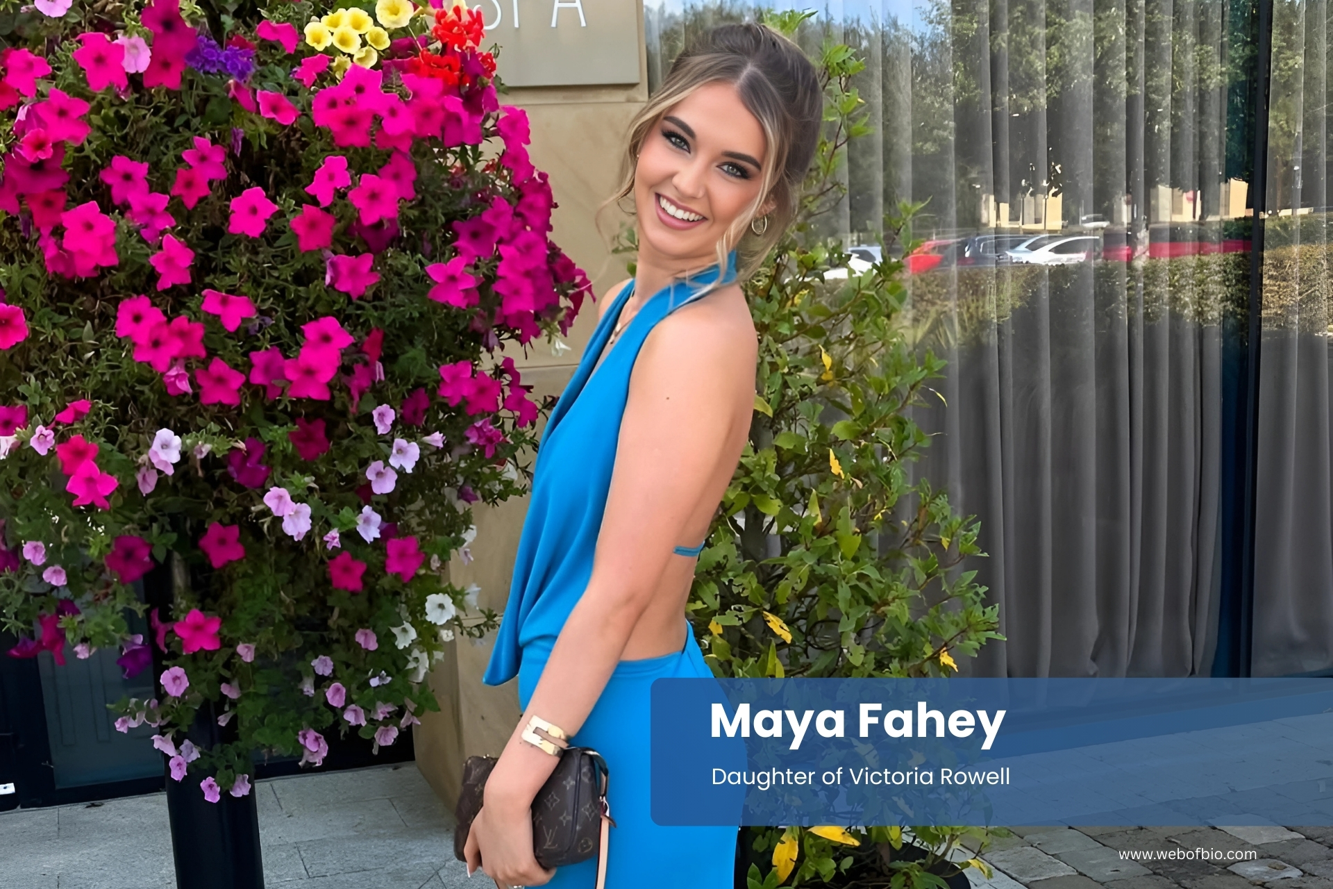 Maya Fahey in a blue dress standing in front of flowers.
