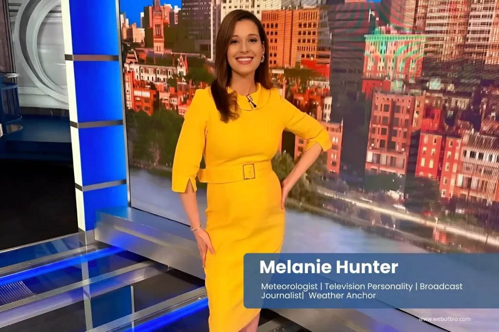 Melanie Hunter in a yellow dress standing on a news set.