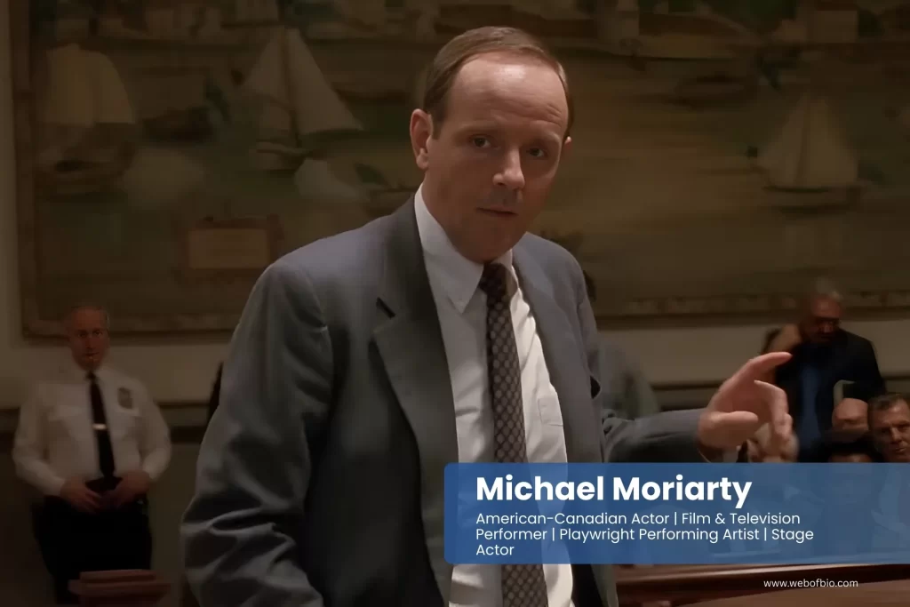 Michael Moriarty in a suit and tie standing in front of a crowd.