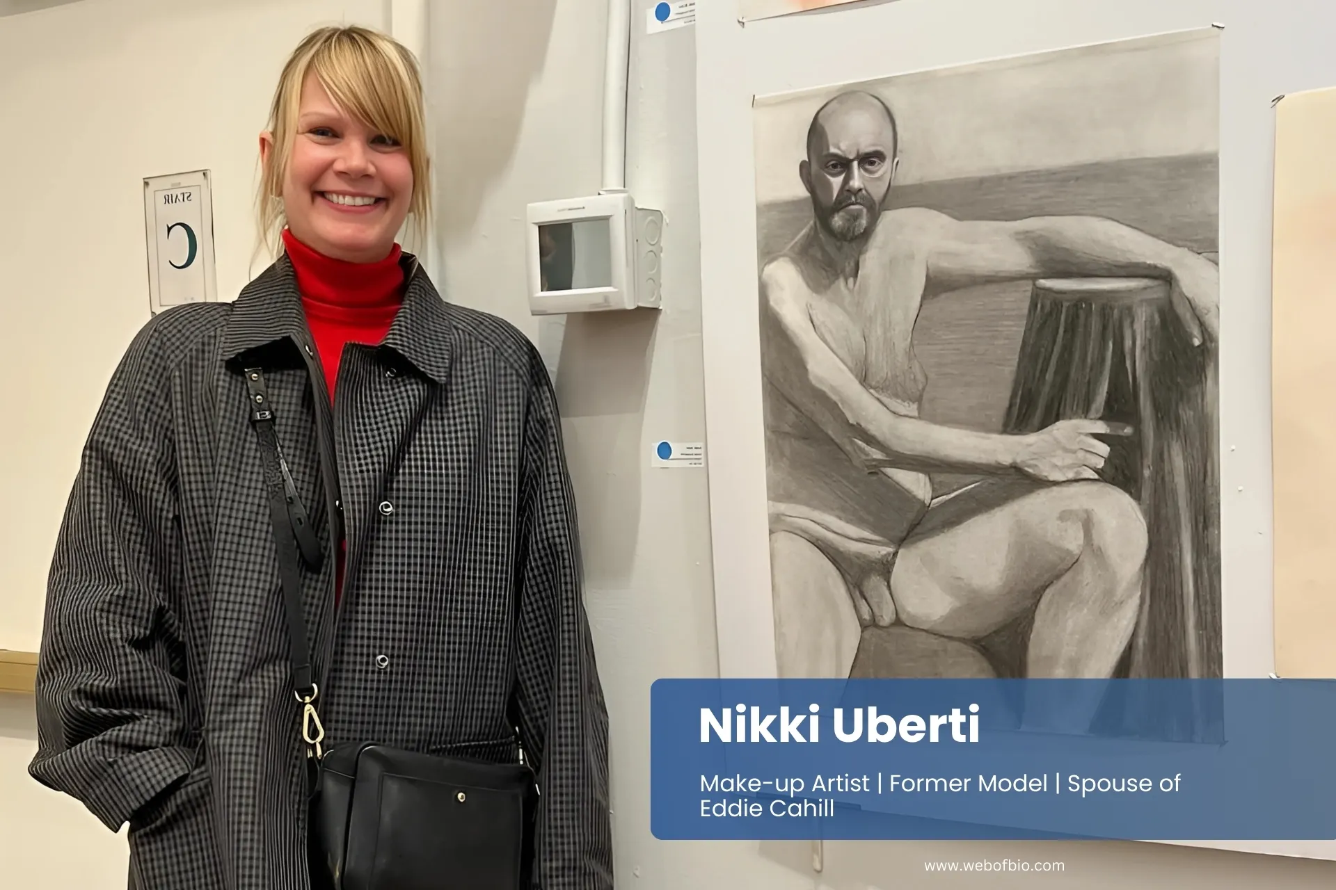 Nikki Uberti stands beside a wall featuring a colorful drawing, smiling as she admires the artwork.