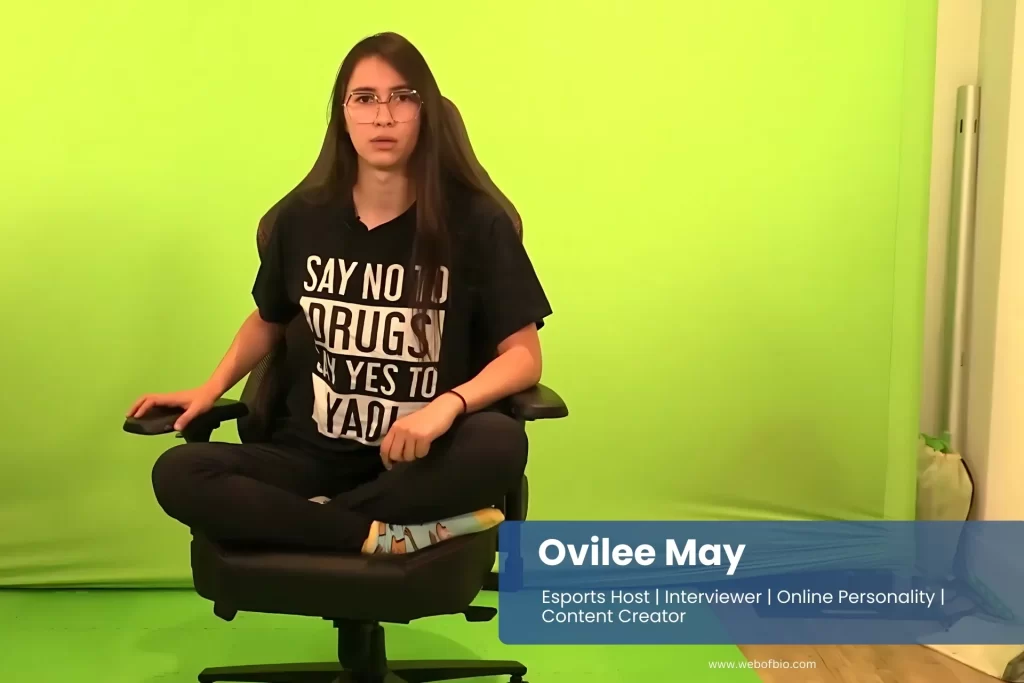 Ovilee May seated in front of a green screen, appearing focused and engaged in her work or presentation.