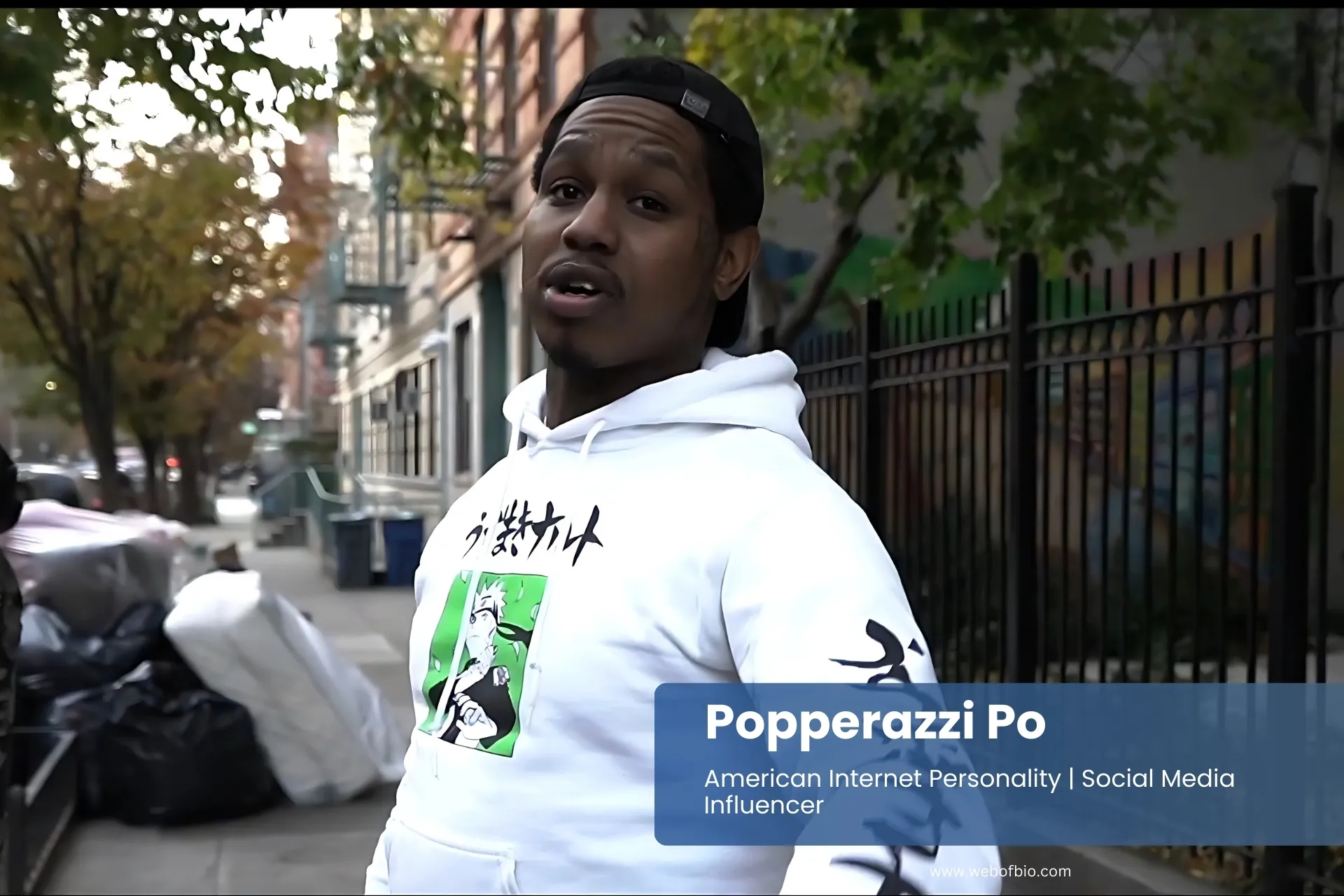 Popperazzi Po wearing a hoodie stands on the sidewalk.