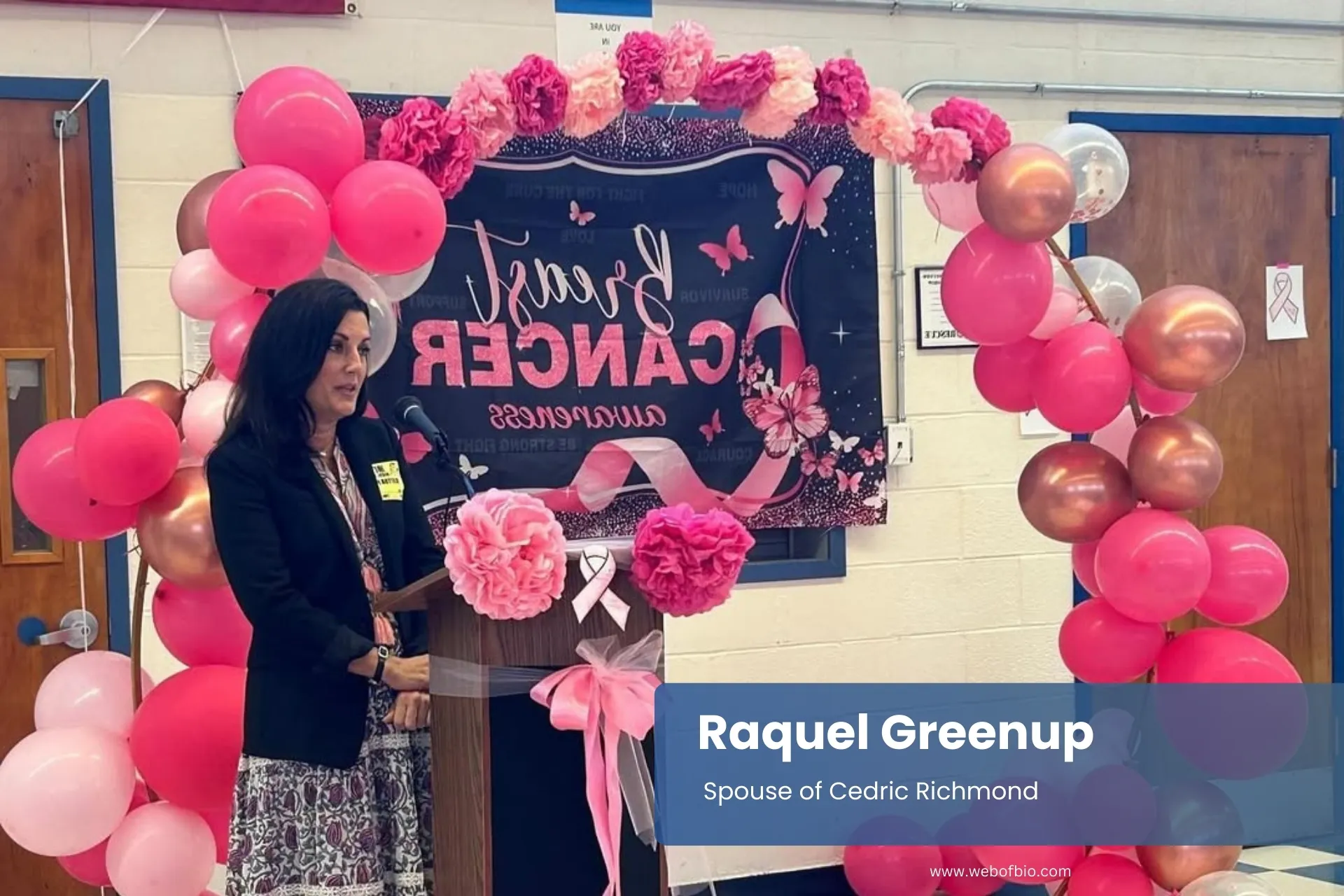 Raquel Greenup speaks at a podium, surrounded by pink balloons.