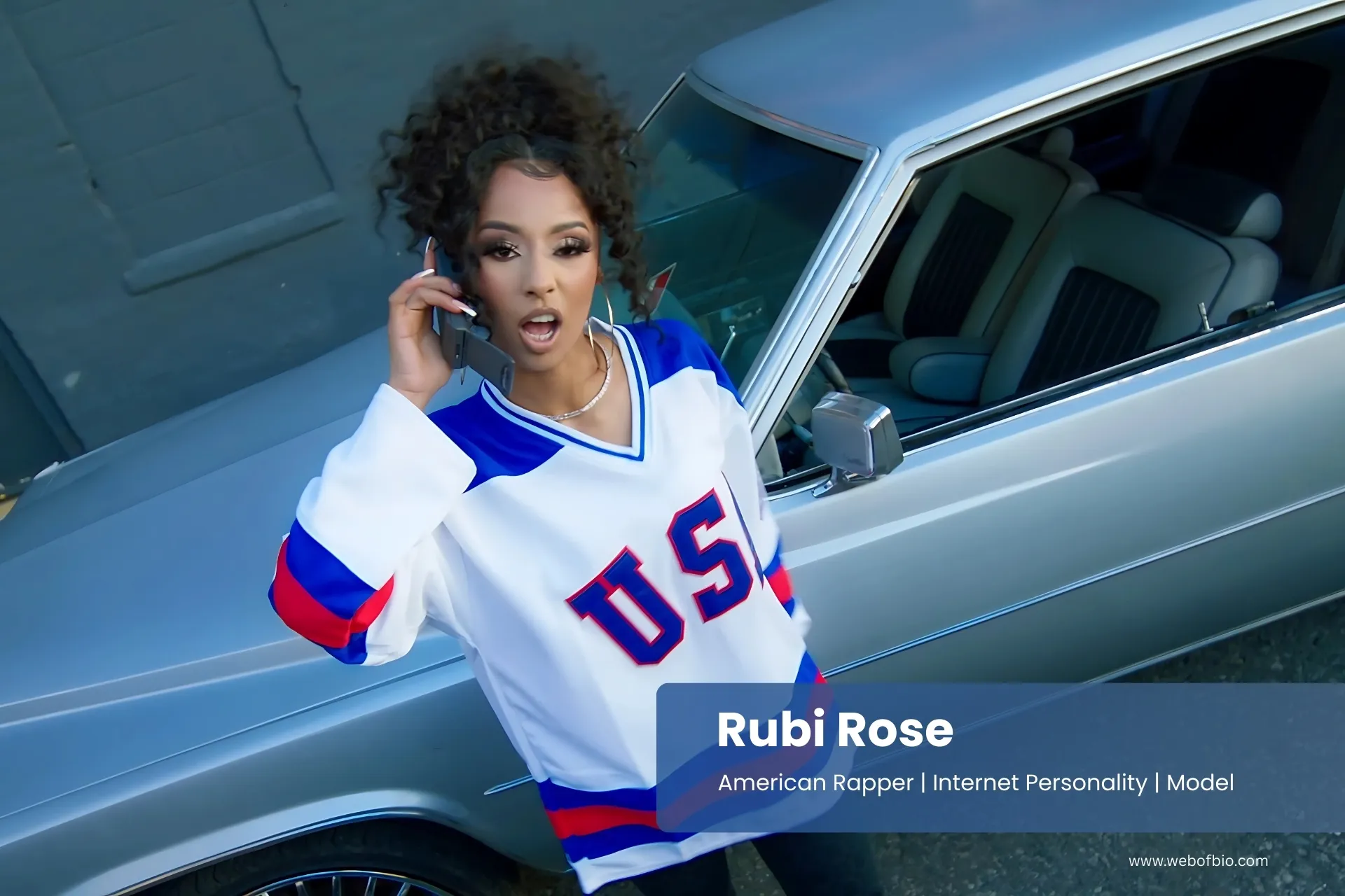 Rubi Rose in a jersey talking on a cell phone next to a car.