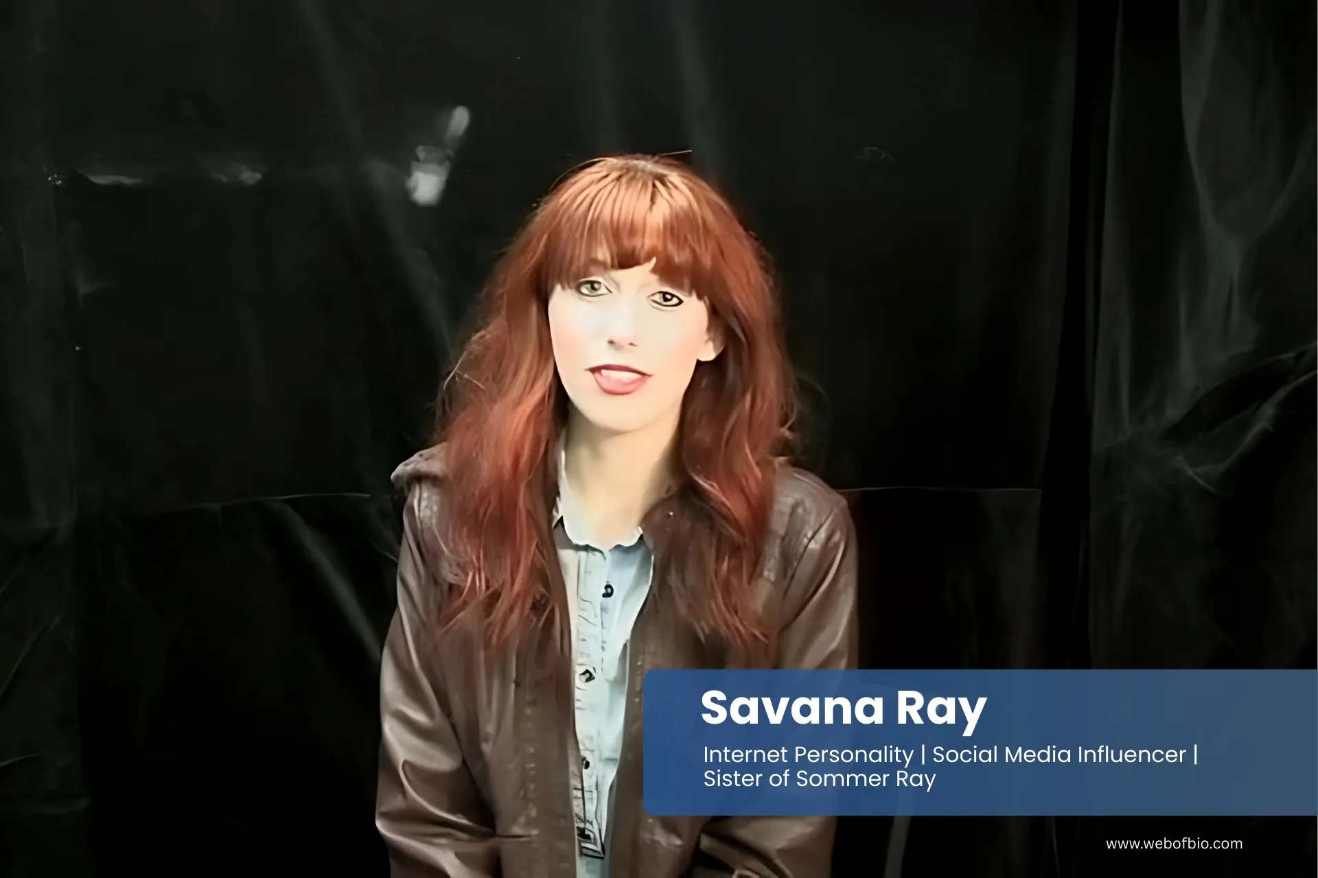 Savana Ray in red hair sitting on a chair in front of a black background.