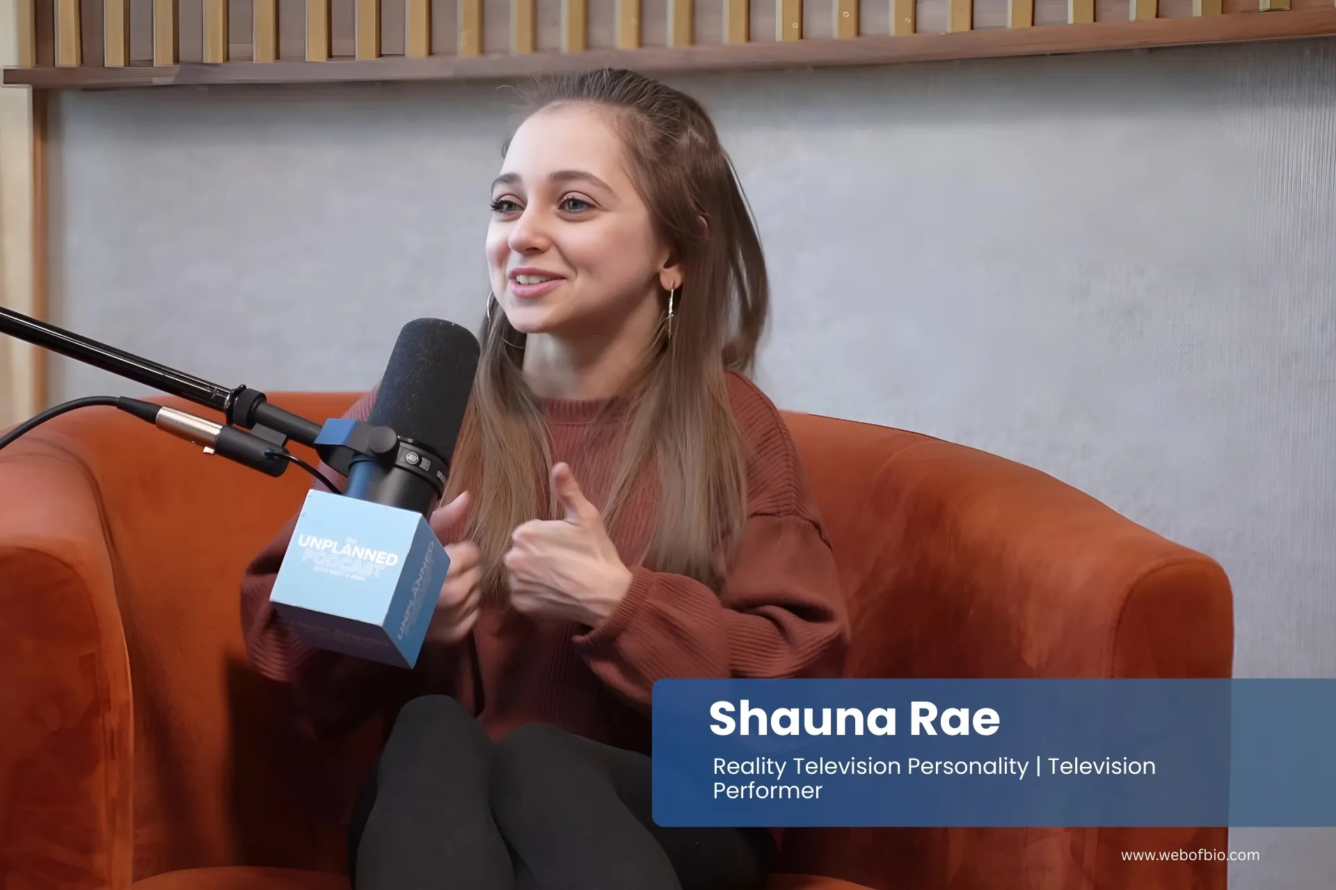 Shauna Rae is sitting in an orange chair with a microphone in front of her.