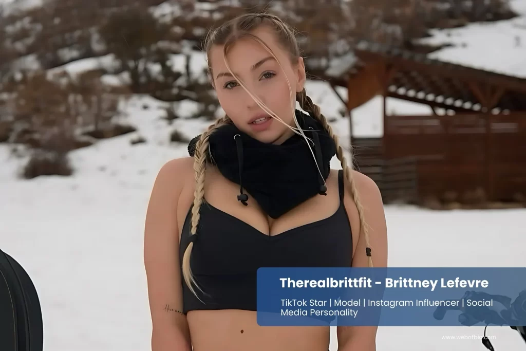Therealbrittfit - Brittney Lefevre in a black bra top standing next to a snowmobile.