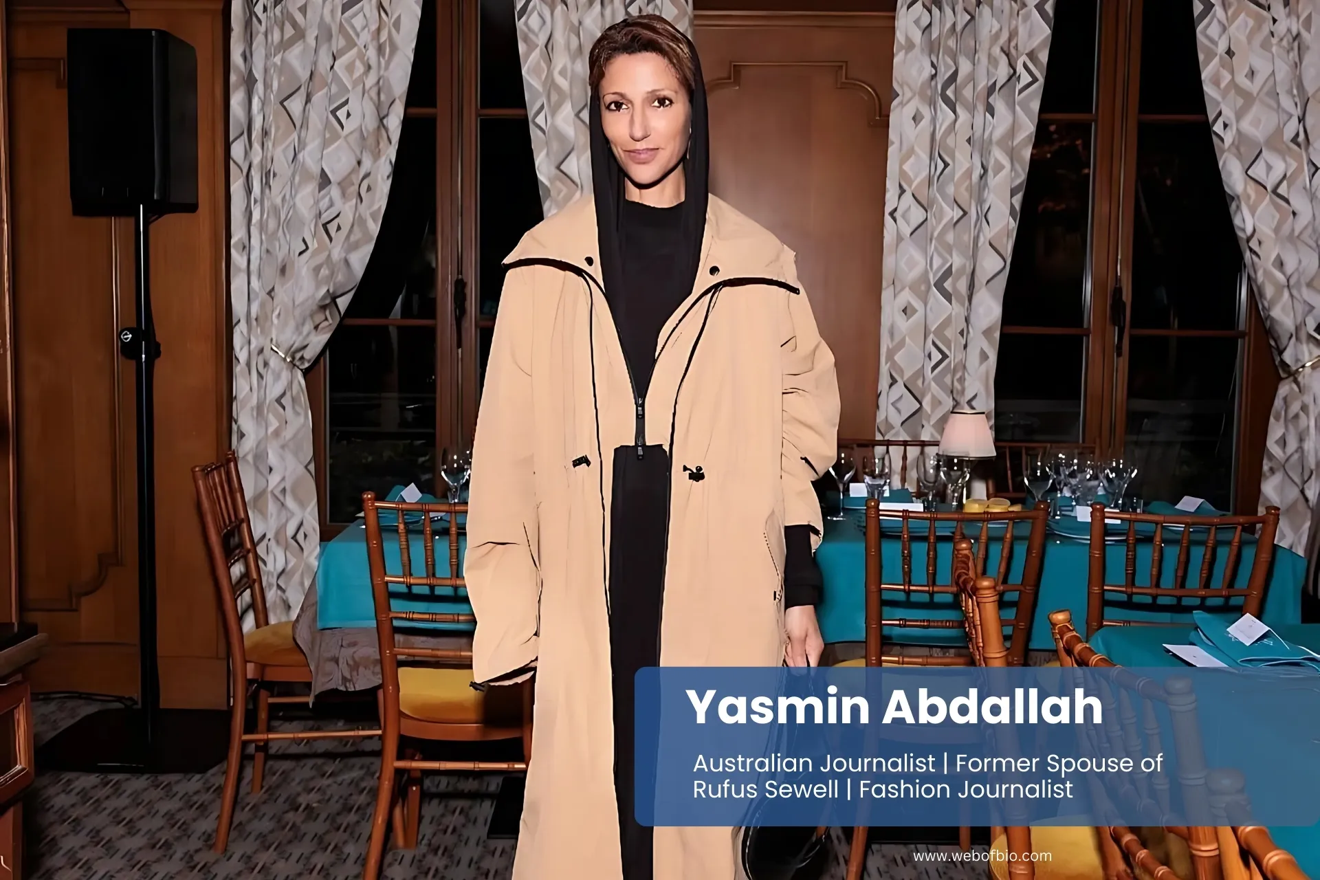 Yasmin Abdallah is in a beige coat and black dress and standing in a dining room.
