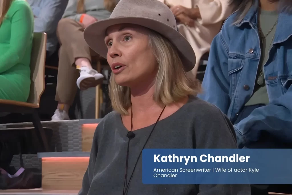 Kathryn Chandler with hat, seated among people.