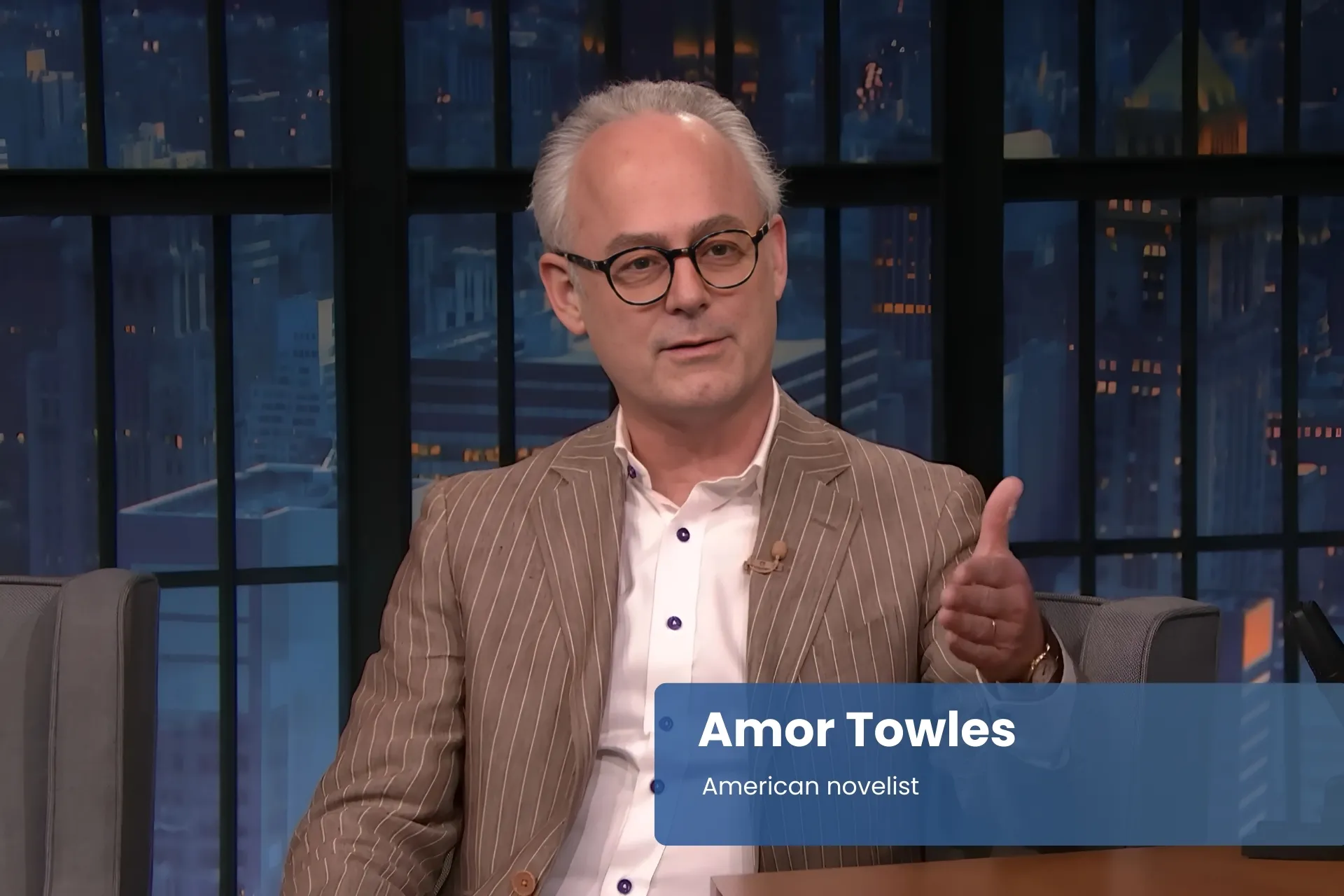 Amor Towles with glasses, seated on television set