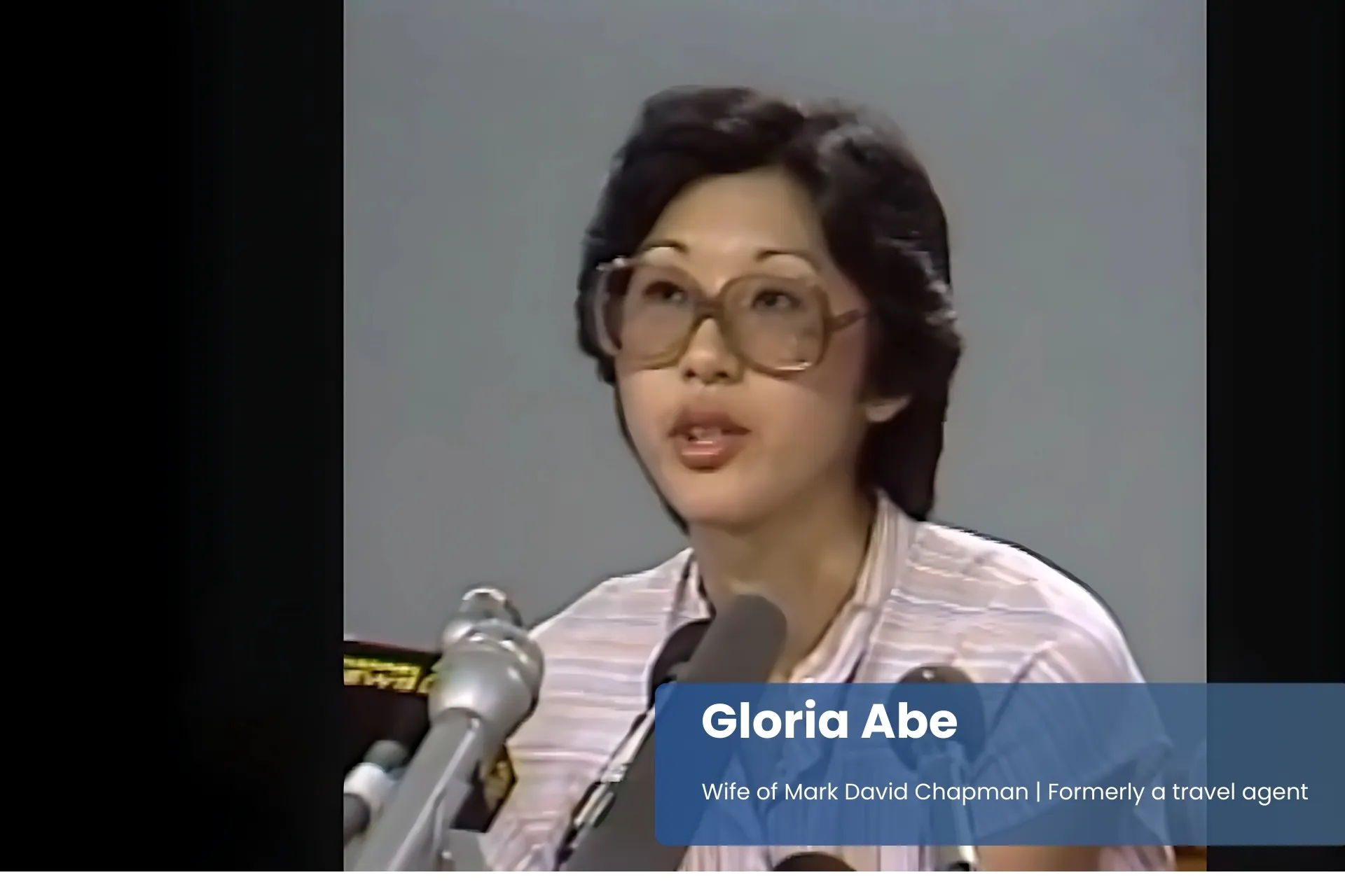 Gloria Abe with glasses, speaking into microphones