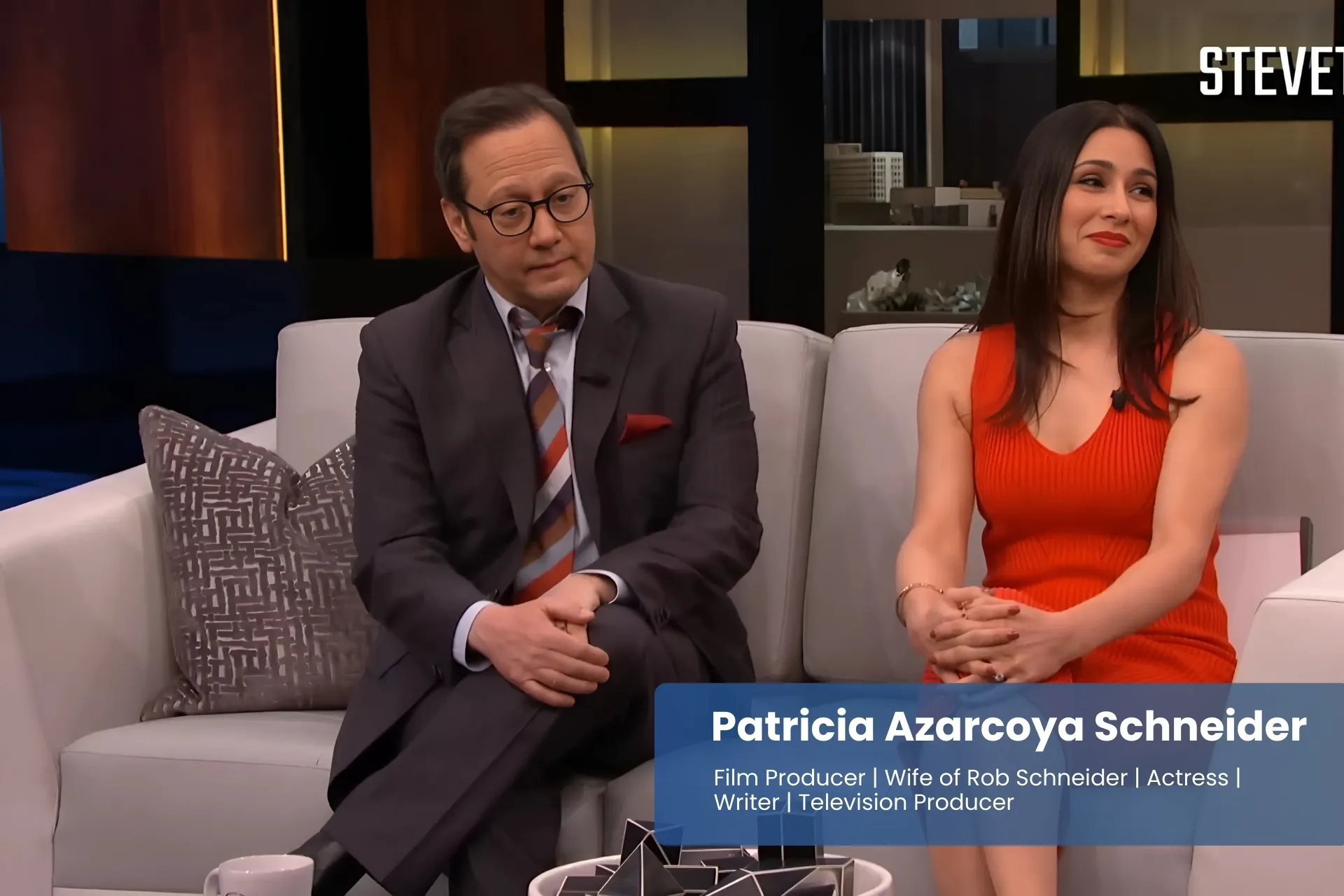 Patricia Azarcoya Schneider and Rob Schneider sitting on couch, talking